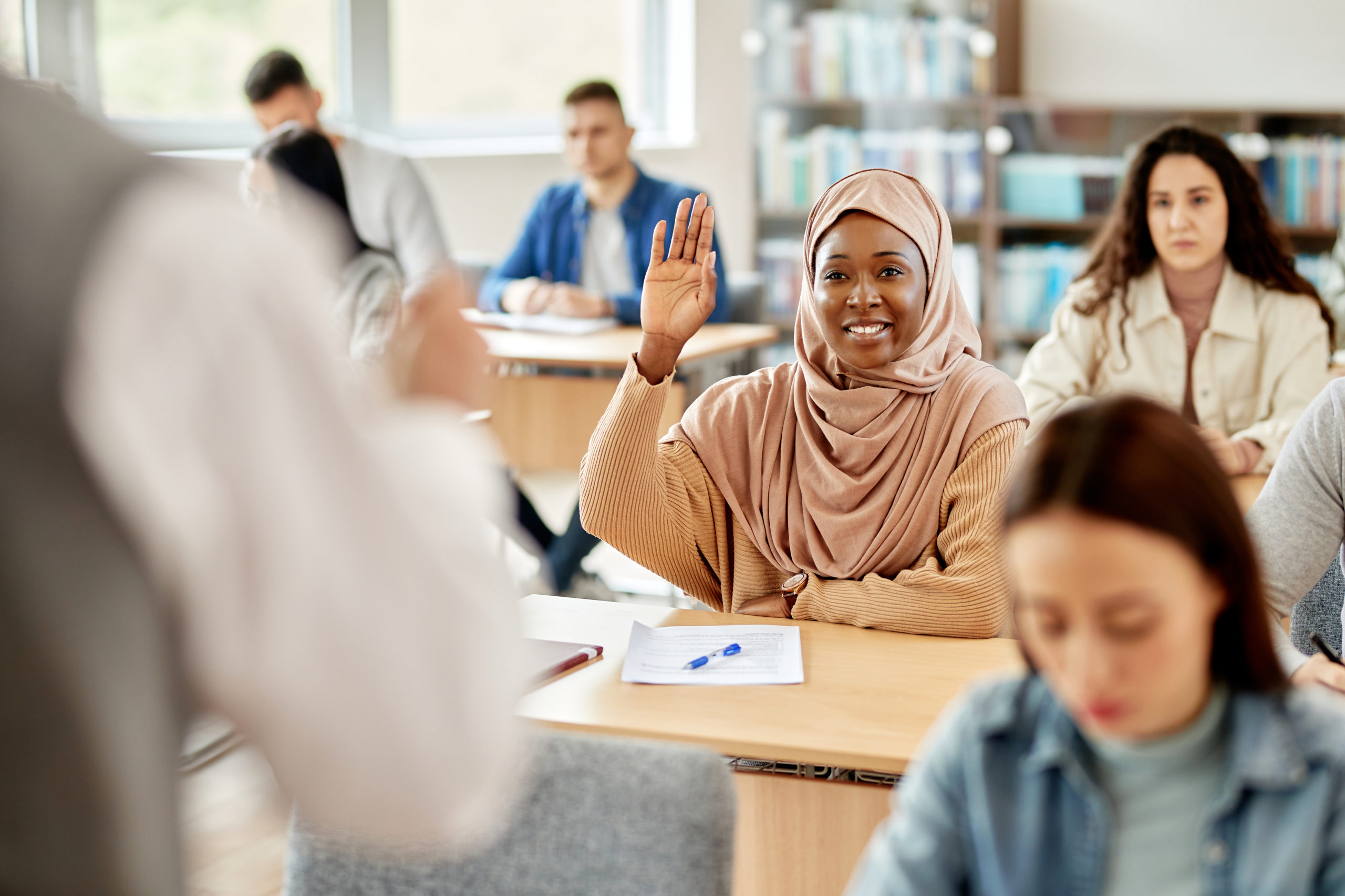 Happy African American student in hijab raising her had to ask a question during lecture at the university.