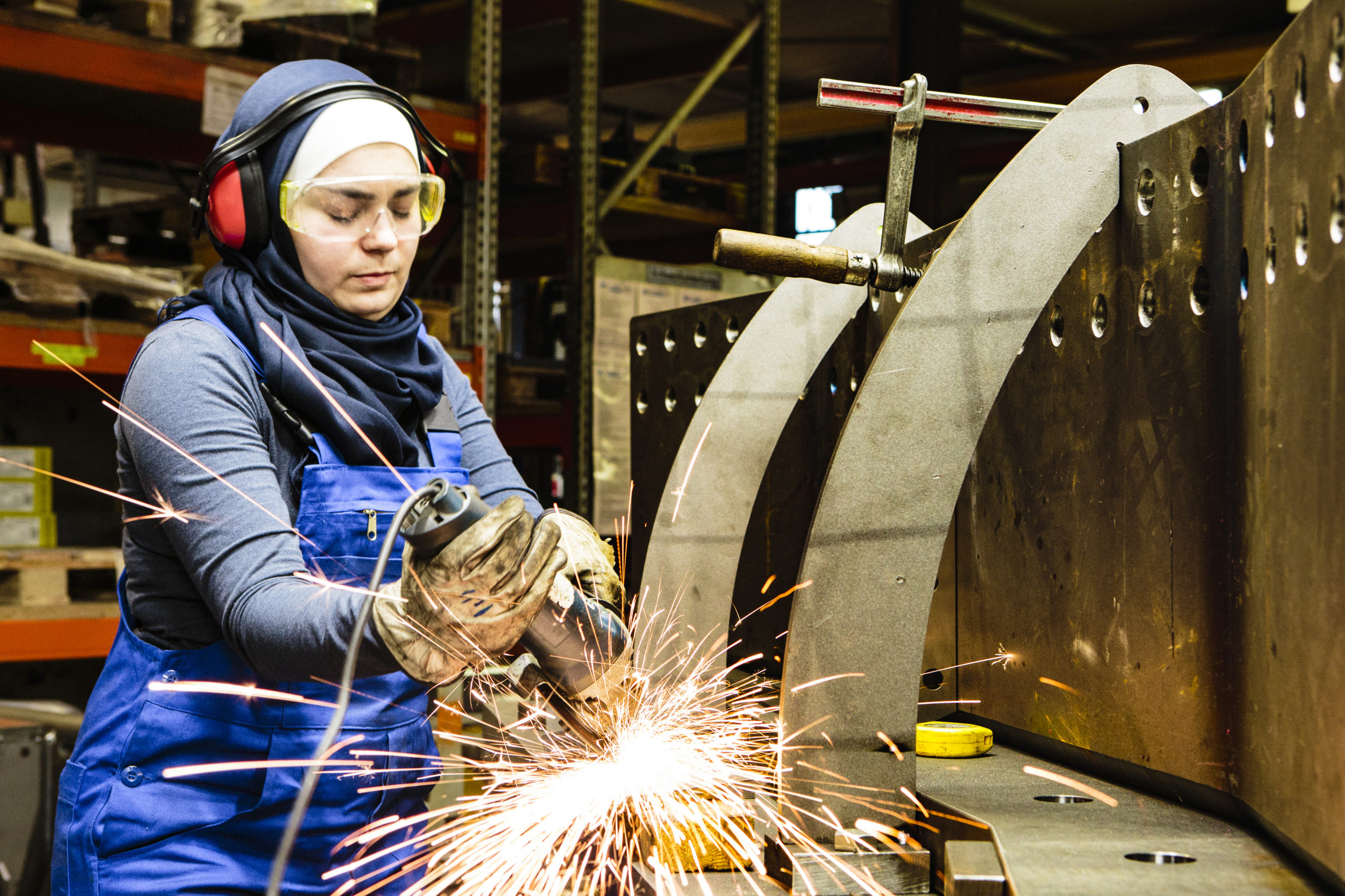 Young female trainee works with a grinder in a workshop, flying sparks