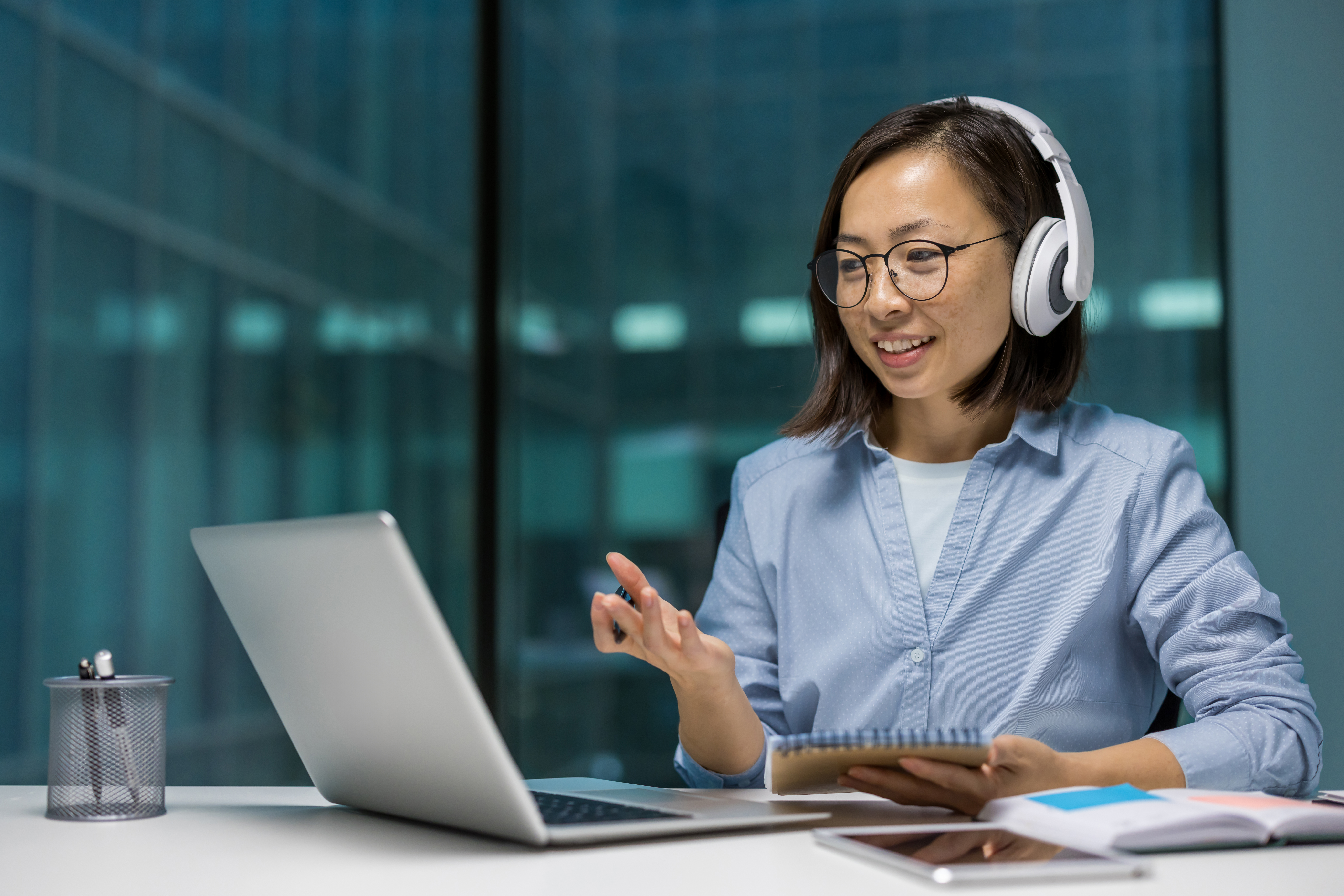 Asian businesswoman with headphones engaged in an educational webinar online course on laptop in modern office setting