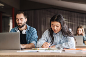 Photo of serious students using laptop and writing in exercise book